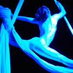 Female acrobat staddles on silks