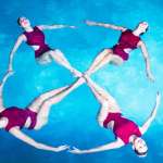 Four female athletes form a flower during a synchronised swimming show in a swimming pool.
